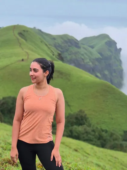 A trekker poses against the backdrop of the stunning green hills and sharp cliffs of the Bandaje landscape.