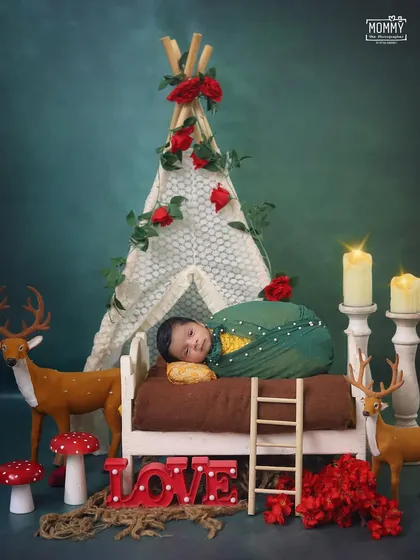 A magical woodland scene with a baby sleeping in a tiny bed. The setup includes a lace teepee, deer figurines, and glowing candles, creating a fairytale atmosphere.