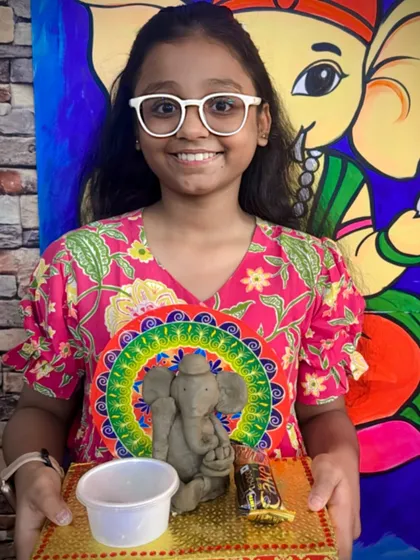 I love seeing the pride on a child's face when they complete their masterpiece. Here, a young artist proudly displays her handmade clay Ganesha idol, sculpted and decorated during our festive workshop. This is a great example of our hands-on clay modeling sessions for kids.