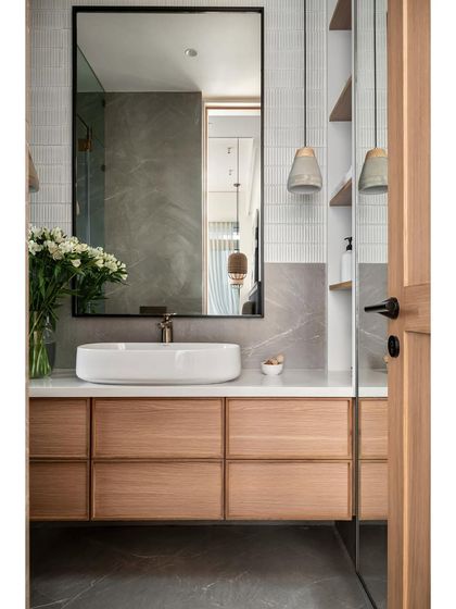 In this master bathroom, a modern aesthetic unfolds through grey matte stone finish tiles and white kitkat tiles. The design highlights a striking white composite marble counter and a mirror framed in black metal.