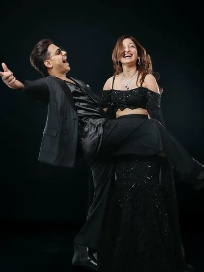 A fun and energetic studio shot capturing a moment of pure joy. The man playfully lifts his partner as they both laugh, showcasing their vibrant chemistry against a classic black backdrop for a dynamic couple portrait.