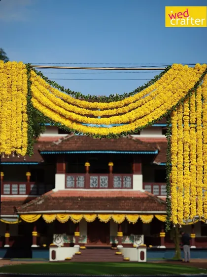 A grand floral arch made of marigolds frames the entrance to a traditional Kerala home, creating a warm and festive welcome for wedding guests.