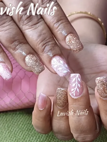A cozy combination of gold and pink glitter nails with a hand-painted white leaf design on a sheer pink base.