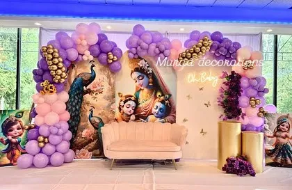 A unique and divine baby shower theme featuring Lord Krishna. The backdrop showcases beautiful artwork of Yashoda and Krishna, framed by a purple and pink balloon garland and a comfortable sofa for the mom-to-be.