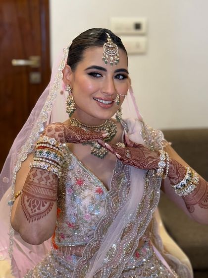 A playful and happy bride ready for her Pheras in a pastel pink lehenga. The makeup is fresh and radiant, with a fun winged eyeliner.