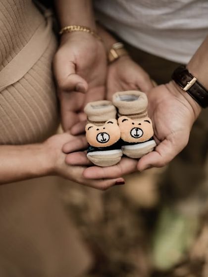 A close-up shot focusing on the tiny bear-themed baby shoes held in the couple's hands. It's an adorable and heartwarming detail for their announcement.