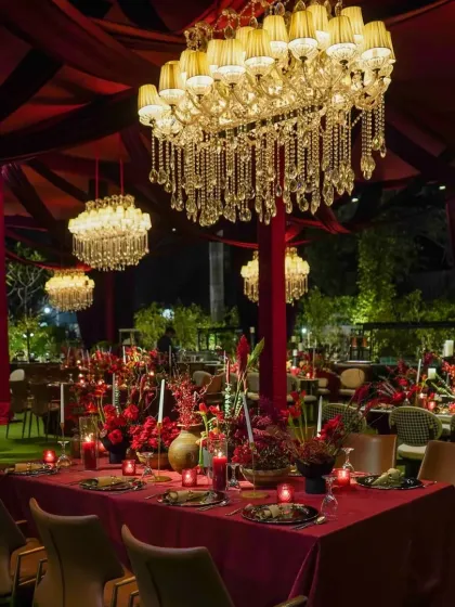The dining setup was designed for drama and intimacy, with long tables draped in deep red linens, abundant red floral centerpieces, and candlelight, all under a canopy of magnificent crystal chandeliers.