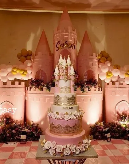 A fairytale cake for a princess's first birthday. This stunning multi-tiered cake, shaped like a castle and adorned with intricate gold details, stands as the centerpiece of a pink palace-themed dessert table, showing how every detail contributes to the story.