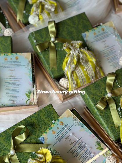 A closer look at a green-themed wedding invitation box. It includes a printed card with all the details, a matching gift box, and a traditional potli bag, all tied together with a satin ribbon.