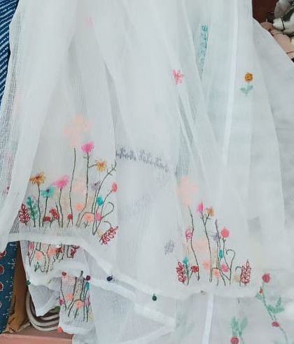 A delicate, sheer white fabric adorned with a field of colourful, hand-embroidered wildflowers.