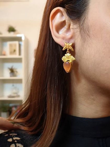 A close-up of the formal embellished drop earrings with an orange stone, perfect for adding a subtle pop of colour.