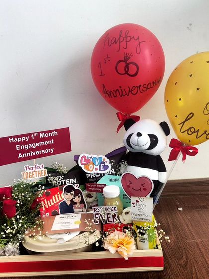 Celebrating a one-month engagement anniversary with this cute and compact hamper. It includes a small bouquet of roses, a panda soft toy, snacks, and personalized balloons.