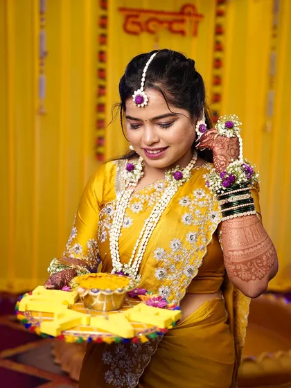 A candid moment of the Haldi bride. The hairstyle is simple yet elegant, allowing the vibrant colors of her outfit and the floral jewelry to stand out.