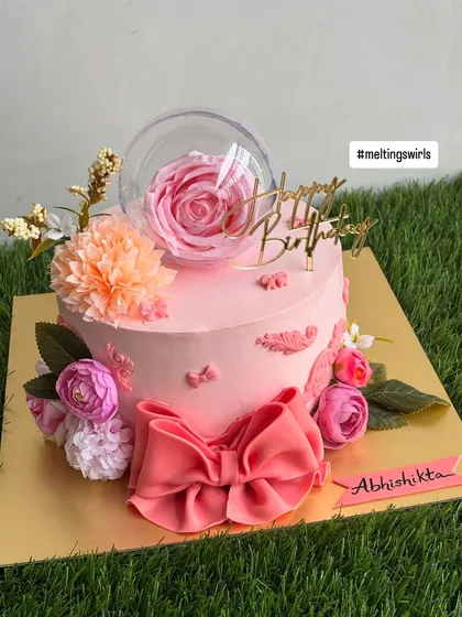 This view shows the beautiful composition of the pink floral cake, with its delicate bow, flowers, and elegant "Happy Birthday" topper.