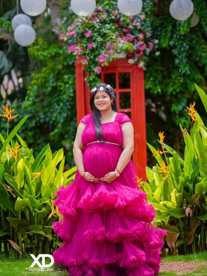 A joyful solo portrait of the mother-to-be in a vibrant pink gown, standing in front of a classic red telephone box.