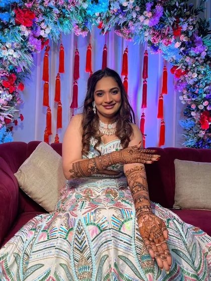 A happy bride in a beautiful lehenga, showing her full-arm bridal mehandi.