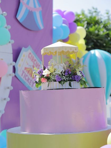 A beautiful floral centerpiece featuring a miniature carousel, set on a tiered stand. This detail adds a touch of elegance to the fun and vibrant carnival theme.