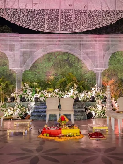 The wedding mandap, set against a backdrop of ethereal white arches and a vertical garden. The minimalist seating and clean lines emphasize the grandeur of the sustainable design, where nature and architecture meet.