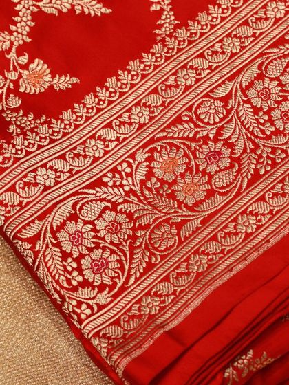 A close-up of the intricate floral motifs woven in gold zari on the red Banarasi saree.