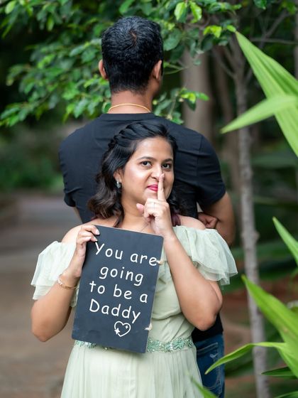 A fun and secret-filled announcement. The mom-to-be holds a sign that says "You are going to be a Daddy" while her partner is turned away.