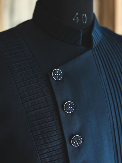 A detail shot of the navy blue Indo-Western jacket, focusing on the custom buttons and the contrast between the smooth fabric and the finely pleated panels.