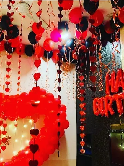 This is an immersive romantic birthday setup in a classic red and black theme. I filled the room with heart garlands, ceiling balloons, and a large heart-shaped balloon frame illuminated with fairy lights for a dramatic effect.