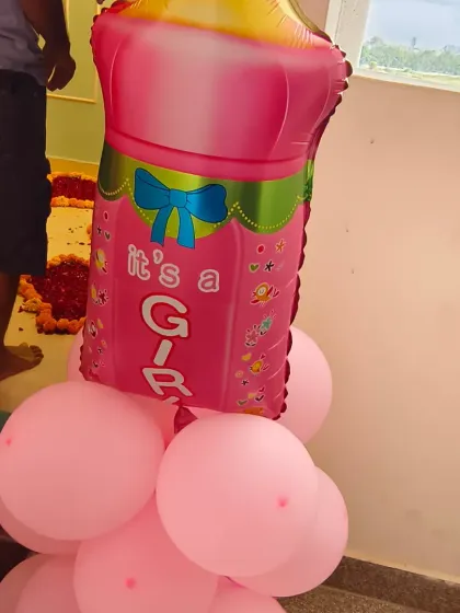 A cute "It's a Girl" foil balloon in the shape of a baby bottle, used as part of a balloon pillar for a welcome home decoration.