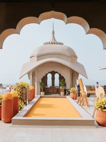 The entrance to the 'Jaipur Wali Haldi', framed by a traditional Rajasthani arch. The path is lined with marigold flowers, setting a festive and welcoming tone for the Mela-themed celebration.