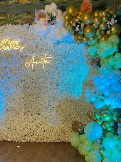 A beautiful 40th birthday setup featuring a full white floral wall, a custom neon sign, and a cascading balloon arrangement in mint green and gold.
