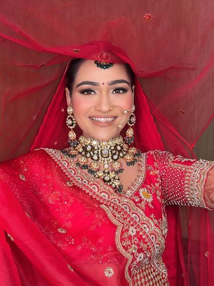 A joyful bride in red. Her smile says it all. The makeup is designed to enhance her happiness, with a radiant glow that lights up her entire face.