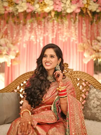 The bride seated on the reception stage, looking like royalty. Her voluminous curls and radiant makeup are the stars of the show.