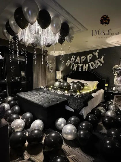 A sleek and modern birthday surprise with a black and silver theme. The dark decor is accented with metallic balloons, fairy lights on the bed, and a "Happy Birthday" banner for a cool, edgy vibe.