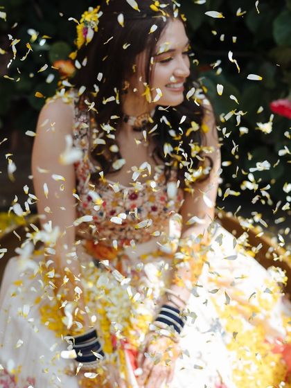 A close-up shot of the bride being showered with white and yellow petals, her eyes closed in blissful joy.