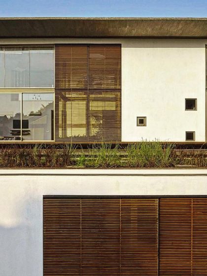 This facade combines different screening elements, including wooden louvers and planters. This layered approach provides varying degrees of transparency and shading, creating a dynamic and functional building envelope.