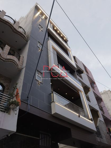 Another perspective of 'The Cursive Abode' facade. This angle captures the interplay between the solid stone wall and the open balconies, framed by illuminated cursive elements.