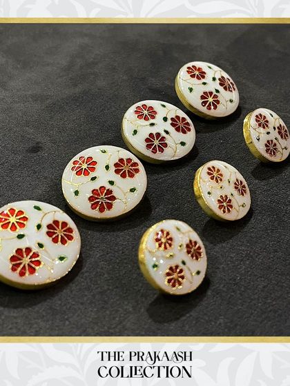 A close-up of our white enamel buttons featuring a delicate red floral pattern with gold detailing. This design is perfect for adding a subtle, elegant touch to both contemporary and traditional outfits.