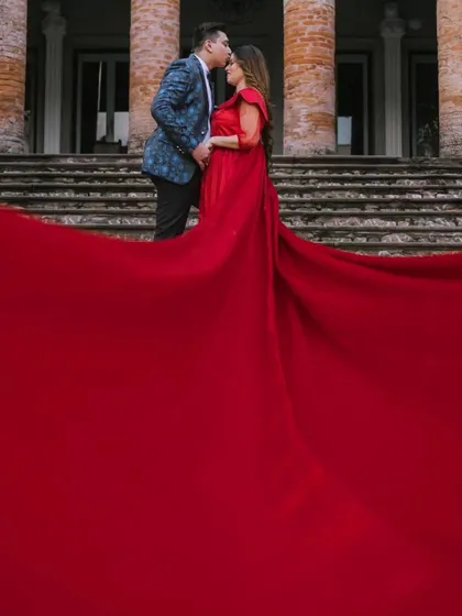 A tender kiss on the forehead, with the massive red trail of the gown filling the foreground. This shot is all about grand romance and intimacy.