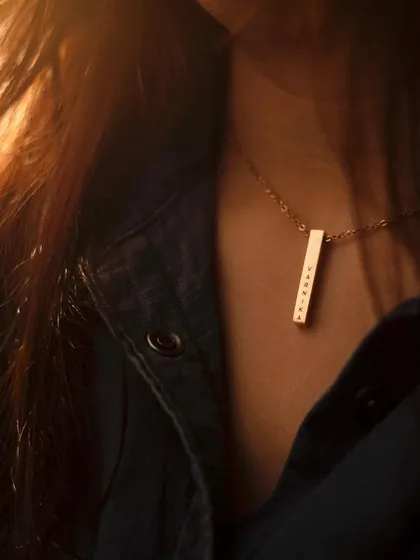 A gold bar pendant with a vertical name engraving, captured in warm, golden hour light. This lifestyle shot shows the necklace as a key part of a stylish, layered outfit.