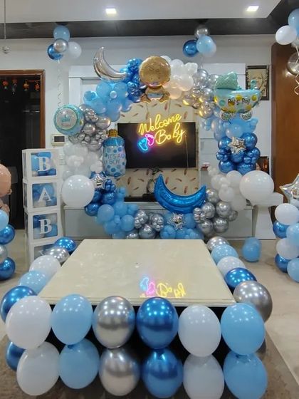 An elaborate living room setup for a 'Welcome Baby' party, with balloons decorating the center table and a large circular balloon arch in the background.