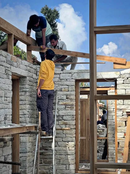 Our team members collaborate on the upper levels of a stone structure in Uttarakhand. Working at height on a sloping site requires immense skill, precision, and trust among the craftspeople.