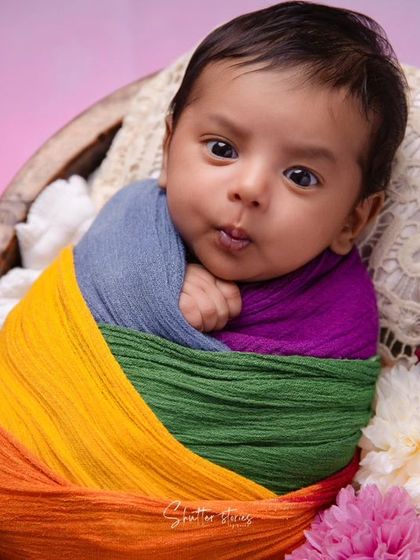 A wonderful close-up capturing the expressive face of the awake rainbow-wrapped newborn.