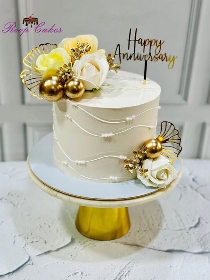 Simplicity and elegance define this beautiful anniversary cake, decorated with white roses and golden accents.