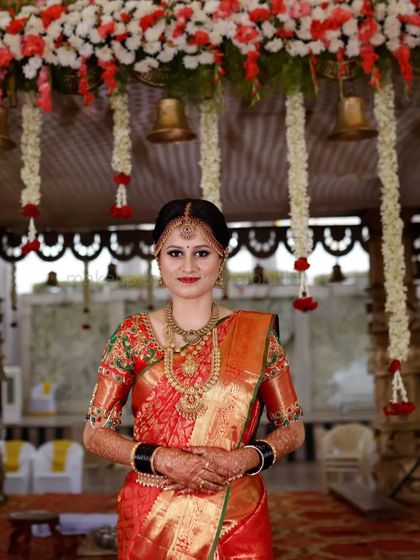 A classic muhurtham look featuring a bright red lip and defined eyes. The traditional matha patti and heavy gold jewellery are perfectly balanced with the makeup, and the bridal braid with fresh flowers is a timeless choice.