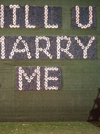 A classic proposal moment captured for a pre-wedding shoot. The "Will U Marry Me" sign made of flowers adds a sweet, romantic touch to the photograph.