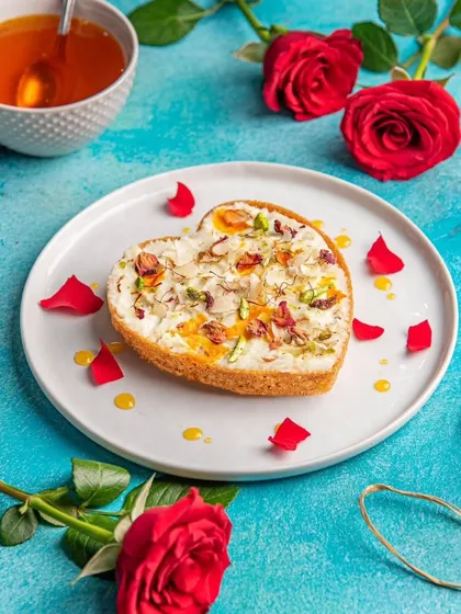 A heart-shaped Ghewar, beautifully decorated with rabri, rose petals, and nuts. A stunning dessert that tastes as good as it looks.