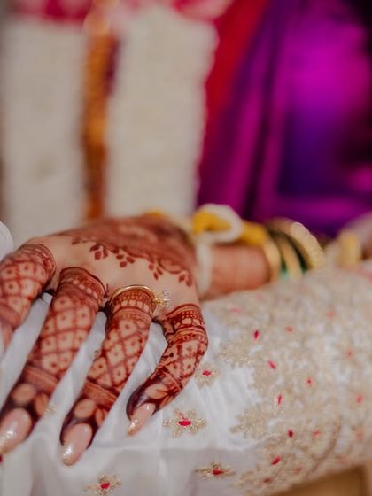 A close-up detail shot of the bride's hand with intricate mehndi, holding the groom's.