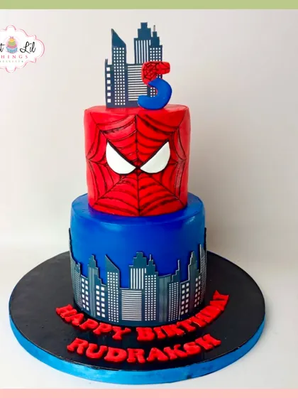 A two-tiered Spider-Man cake for a 5th birthday. The top tier features Spidey's mask, while the bottom tier shows a city skyline, creating a dynamic superhero scene.