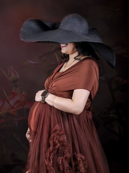 A chic and mysterious solo portrait. The oversized hat adds a touch of high fashion and drama, while the profile pose highlights the baby bump.