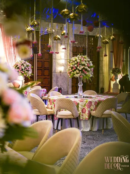 A guest table at the Sufi-inspired engagement. The floral-printed tablecloth is complemented by a tall centerpiece of pink and white roses, while hanging floral tassels add a traditional touch.