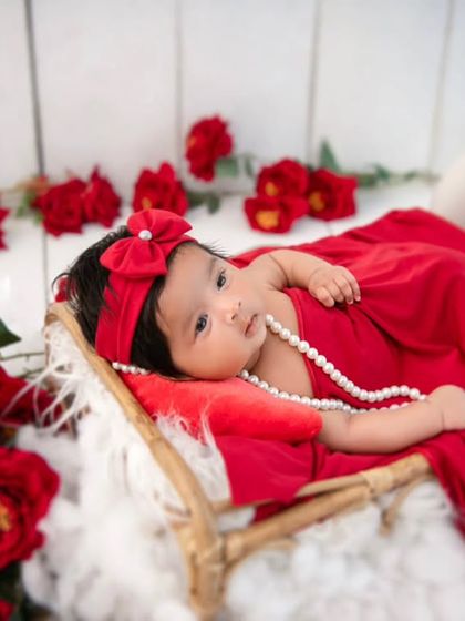 A newborn rose. This dramatic portrait of a newborn in a red wrap, surrounded by red roses, is a powerful and artistic way to announce her arrival.